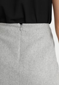Jupe grise en feutre, à coupe droite, avec fermeture éclair au dos et texture lisse. Design simple sans motifs ni accents.