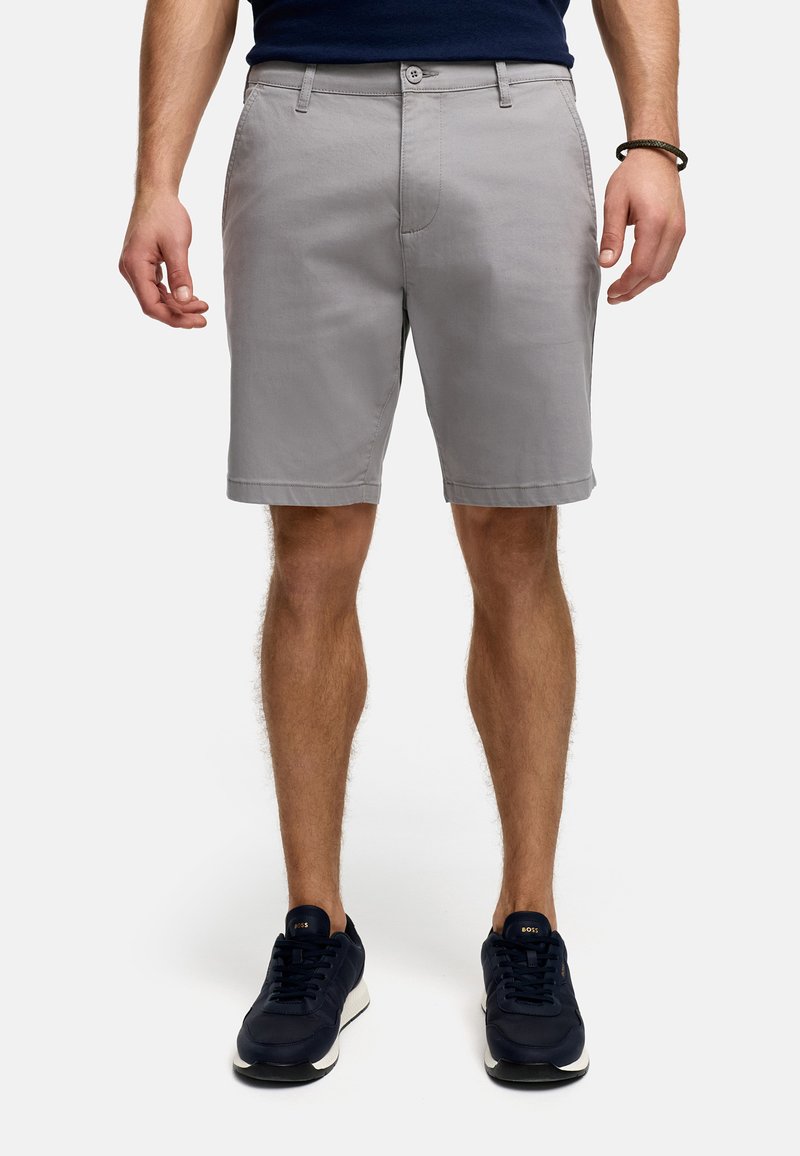 Grå bomullsshorts med en platt framsida, bältesöglor och sidfickor. Matchas med mörkblå sneakers.