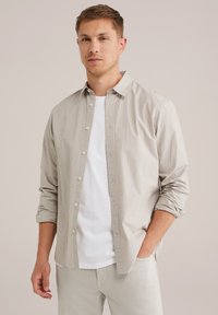 Lichtgrijs en witte gestreepte button-up shirt van zacht stof, met een puntige kraag en opgerolde mouwen. Draagt over een wit T-shirt.