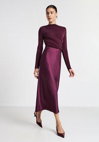 Abito lungo bordeaux con maniche lunghe, dotato di un torso aderente e una superficie in satin liscio, caratterizzato da un design drappeggiato e una gonna dritta lunga fino al pavimento.