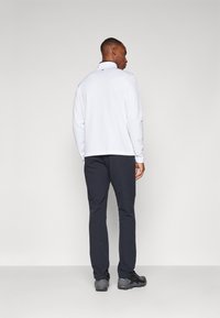 Chemise blanche à manches longues avec un col montant, associée à un pantalon gris foncé et des chaussures noires. Design simple, texture lisse et coupe ajustée.
