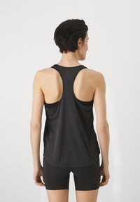 Top desportivo preto com design de costas nadador, apresentando um corte solto, tecido leve e uma barra arredondada, combinado com calções pretos.