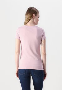 T-shirt in cotone rosa chiaro con maniche corte, forma aderente e scollo rotondo. Texture liscia, senza motivi visibili o elementi metallici.