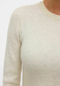Hellbeige gerippter Strickpullover mit rundem Ausschnitt und langen Ärmeln, der eine weiche Textur und einen leichten Stretch im Gewebe zeigt.