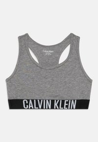 Sivi atletski grudnjak s dizajnom na leđima. Ima crni elastični pojas s bijelim tekstom "Calvin Klein". Mekani materijal i prilagodljiv oblik.