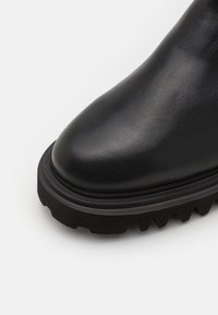Stivale ankle in pelle nera con punta arrotondata, superficie testurizzata e suola spessa in gomma nera rugged con battistrada prominente.