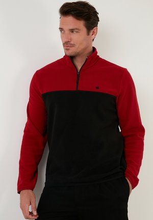 Red and black zip-up fleece pullover with long sleeves, black chest panel, and small logo on the left side. Smooth texture.