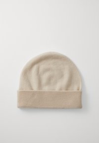 Beige strikket lue, avrundet topp og ribbet mansjett. Myk tekstur, minimal design, uten synlige mønstre eller merker.