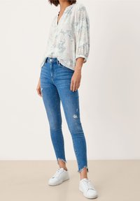 Haut léger à motifs dans des tons pastels, associé à un jean skinny bleu déchiré et à des baskets blanches à semelle texturée.