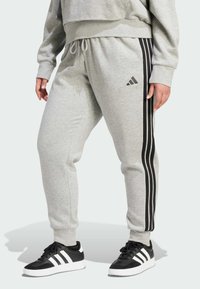 Harmaat verkkarit mustilla raidallisilla yksityiskohdilla, joustava vyötärö ja resorit nilkoissa. Yhdistetty mustiin ja valkoisiin tennareihin, joissa on kolme raitaa.