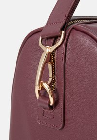 Burgundy leather handbag featuring a gold-tone hardware clasp, smooth texture, and a zip closure with detailed stitching accents.