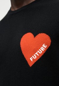 Pull en tricot noir avec un motif de cœur rouge et le mot « FUTURE » en texte blanc au centre. Texture lisse, coupe ajustée.