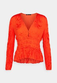 Blouse froissée à manches longues orange vif, avec un profond décolleté en V et une taille froncée, créant un ourlet péplum légèrement évasé.