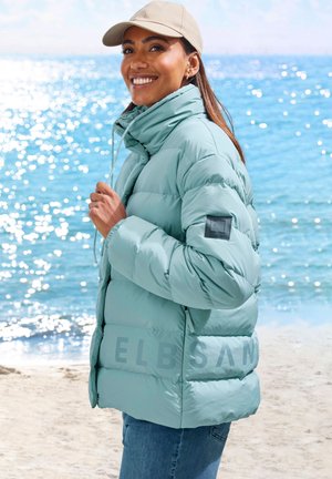 Light blue puffer jacket with a high collar, zipper, and elastic cuffs. Features branded text on the side and is worn over denim jeans.