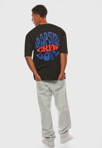 Sort oversized t-shirt med blåt og rødt grafisk tekst "DROPSIZE CREW GOLF" på ryggen. Kombineret med lysegrønne bukser og hvide sneakers.