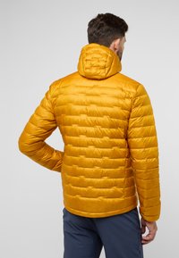 Veste matelassée de couleur jaune vif avec une capuche, dotée de sections matelassées et d'une texture lisse. Idéale pour les activités en plein air.
