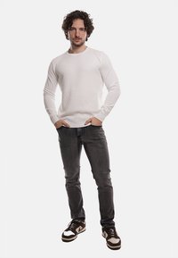 Maglione bianco a trama con scollatura rotonda, abbinato a jeans scuri e sneakers nere. L'outfit presenta una vestibilità slim e dettagli a coste.
