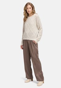 Hellbeige gestrickter Pullover mit einem Rautenmuster, kombiniert mit weiten, taupefarbenen Satin-Hosen und cremefarbenen Ankle-Boots.