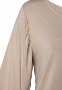 Top beige morbido e leggero, con maniche arricciate e scollatura rotonda. Tessuto liscio con dettagli minimi.