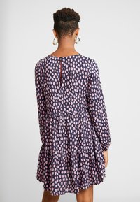 Blommönstrad klänning med marinblå bakgrund och rosa accenter, långa ärmar, en lager-på-lager fåll och en nyckelhål-design på ryggen.