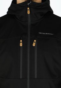 Black softshell jacket with a zippered front, two chest pockets, and a hood. Features contrast stitching and a logo on the chest.
