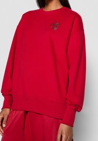 Felpa rossa con maniche lunghe e polsini a coste. Presenta un design testurizzato "LOVE" sul petto. Realizzata in una morbida miscela di cotone.