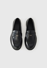 Black leather loafers with a sleek design, featuring a broad strap and gold logo accent. Textured sole and smooth finish.