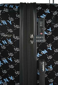 Maleta negra con un acabado brillante, patrón de logo DKNY en azul y gris, dos cremalleras y un candado de combinación en el lateral.