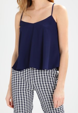 Navy blue camisole with thin straps, relaxed fit, and flowing design, paired with patterned black and white checkered pants.