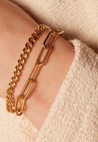Gouden armbanden met een gladde, ronde kettingontwerp en een grotere schakelketting. Beide zijn metallic en gestructureerd.