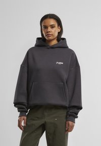 Mørkegrå oversized hoodie lavet af bomuldsblanding, med en frontlomme og et lille hvidt logo, samt en hætte med snoretræk og ribbede manchetter.