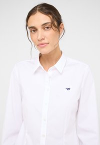 Biała koszula zapinana na guziki, wykonana z bawełnianej tkaniny, z kołnierzykiem, długimi rękawami i małym niebieskim logo konia na lewej piersi.