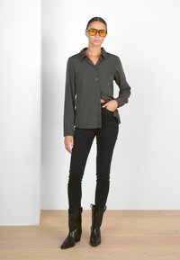 Camicia button-up verde scuro, jeans skinny neri, stivali da cowboy neri e occhiali da sole arancioni. Tessuto morbido e design aderente.
