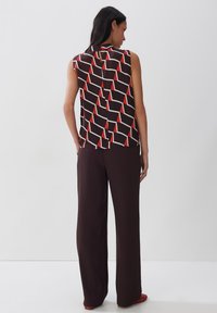 Mouwloos topje met een geometrisch patroon van rode en witte driehoeken op een donkere achtergrond, gecombineerd met donkere wijde broek.