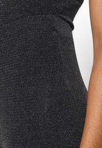 Svart klänning med ett texturerat, glittrigt tyg. Tät design med en mjuk yta, subtil lyster och rena linjer som framhäver formen.