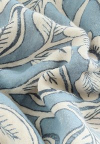 Blue and cream fabric featuring a floral pattern with swirling leaves, made of textured material, soft and wrinkled appearance.