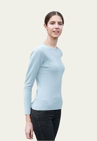 Haut bleu clair à manches longues, silhouette ajustée, texture lisse, encolure ronde, associé à un jean foncé. Pas de motifs ou d'accents distinctifs.