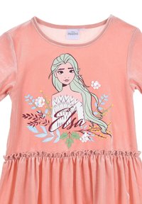 Abito rosa in velluto con vita arricciata, maniche lunghe e un'immagine di un personaggio con capelli lunghi, accenti floreali e testo in basso.