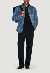 Camicia di jeans con colletto classico, colore azzurro chiaro e finitura testurizzata, abbinata a pantaloni cargo neri e sneaker nere.