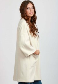 Cappotto oversize crema realizzato in tessuto morbido, con maniche a tre quarti, taglio dritto e tasche laterali. Texture liscia, con minimalismo nei dettagli.