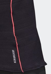 Musta urheilutoppi, jossa on kontrastivärinen vaaleanpunainen sauma sivussa ja "AEROREADY" -logo helman kohdalla. Sujuva, kevyt kangas.