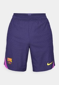 Vijolične športne kratke hlače z mrežastim vzorcem, ki vsebujejo logo FC Barcelone in roza stranski trak. Nike logo v rumeni barvi se nahaja v spodnjem desnem kotu.