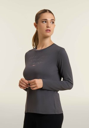 Maglietta grigia attillata a maniche lunghe con scollatura rotonda. Presenta dettagli testuali riflettenti sul petto. Realizzata in un materiale liscio e elasticizzato.