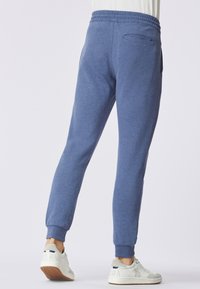 Pantaloni jogger in pile blu con polsini a costine e vita elastica. Presentano una tasca posteriore e sono abbinati a sneakers bianche.