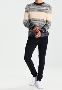 Gebreide trui met horizontale roomkleurige en marineblauwe strepen, ronde halslijn, geribbelde boorden, gecombineerd met een donkere spijkerbroek en witte sneakers.