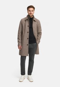 Bruine wolmix jas met een kraag, frontknopen, gecombineerd met een zwarte trui, grijze broek en witte sneakers. Neutrale tinten, klassiek ontwerp.