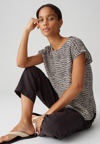 Zwart en crèmekleurig patroon, kortemouwen top met een ronde hals, gecombineerd met losse zwarte broek en beige slippers. Glad stofmateriaal.