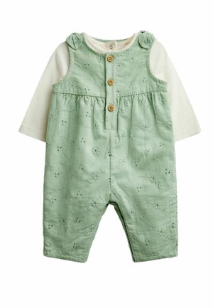 Combinaison bébé en velours côtelé vert avec boutons sur le devant et motif floral ajouré, superposée à un t-shirt crème à manches longues avec fermeture par boutons au col.