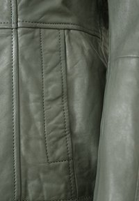 Grüne Lederjacke mit vertikalen Nähten, strukturiertem Oberflächenbild und dezentem Glanz. Verfügt über gesteppten Akzente an den Ärmeln.