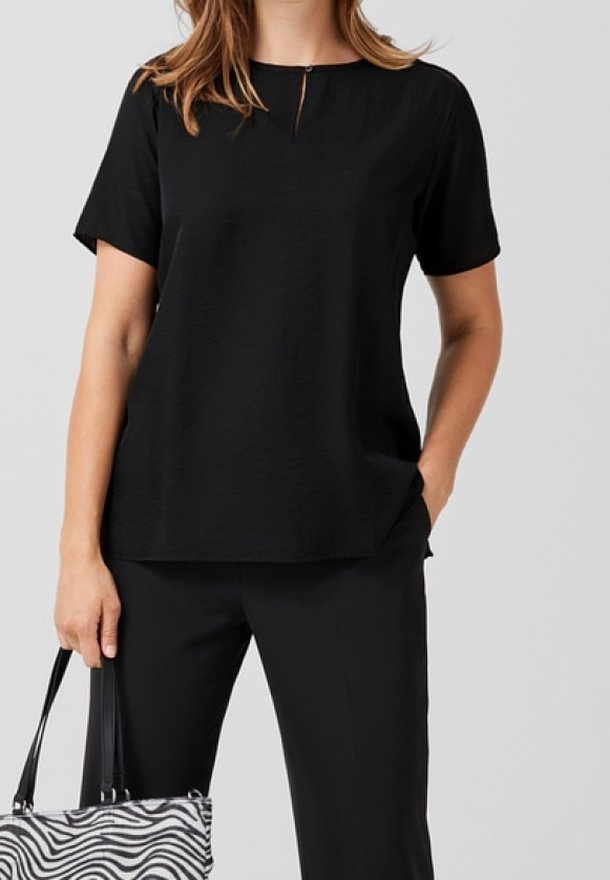 Femme portant un haut noir à manches courtes et un pantalon, tenant un sac à main imprimé zèbre noir et blanc, avec une main dans la poche.